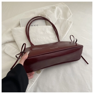 Detail of burgundy underarm bag with bow accents and Fashion & Bags text on glossy leather