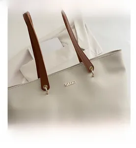 Close-up of cream tote bag featuring brown leather handles and a gold metal logo plate