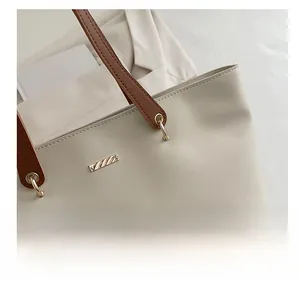 Close-up of minimalist cream tote bag with brown straps and golden metal hardware detail