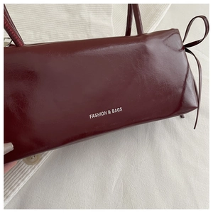 Close-up of wine red baguette bag with glossy leather texture and bow detail