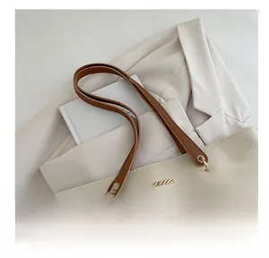 Detail of minimalist tote bag showing gold hardware accents and brown leather handles