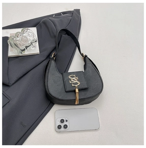Macro detail of black crescent shoulder bag with golden logo and tassel on grey blazer