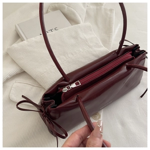 Detail of dark red glossy leather underarm bag with side bow on corduroy background