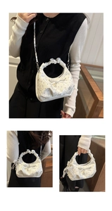 Close-up of white ruched handbag with lace embroidery, pearls and silver chain detail