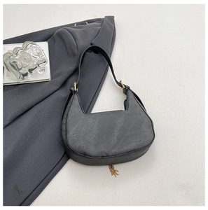 Detail of black crescent shoulder bag featuring gold buckle and metal chain fringe