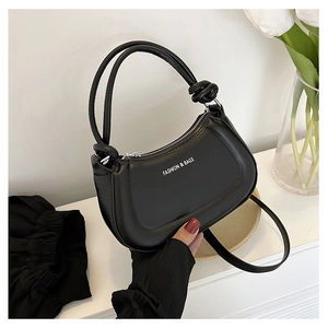 Detailed view of black matte leather crescent bag with knot strap and white fashion text