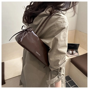 Detail of dark brown glossy leather shoulder bag with chic bow accent and long straps