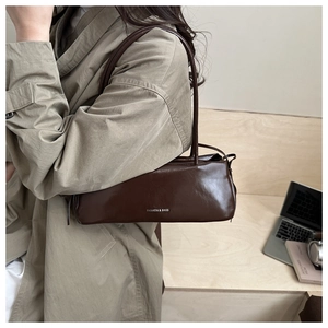 Detail of dark brown glossy leather baguette bag with 'FASHION & BAGS' text on shoulder