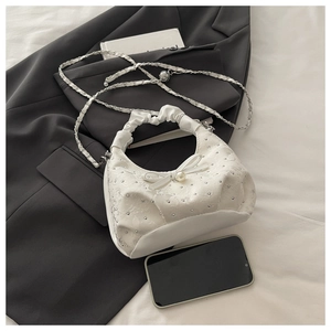 Close-up of white sequined handbag with pearl bow and ruffled handle on gray blazer