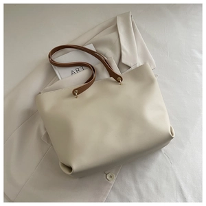 Detail view of cream tote bag with brown leather straps on a beige blazer background