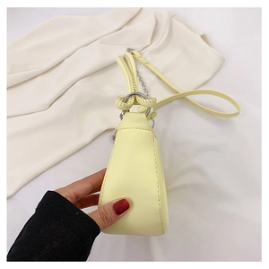 Detail of cream yellow leather crossbody bag featuring a twisted handle and metal rings