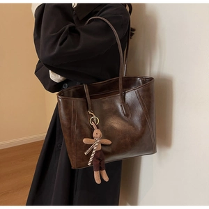 Detail of dark brown tote bag with glossy finish and cute plush rabbit charm accessory
