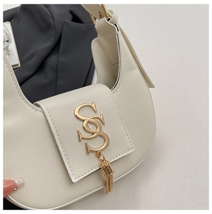 Detailed macro of cream-white crescent shoulder bag featuring gold SS logo and tassel