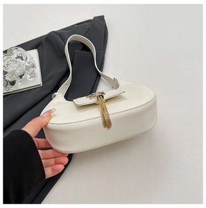 Close-up of white lychee leather half-moon bag with elegant gold tassel and metal buckle