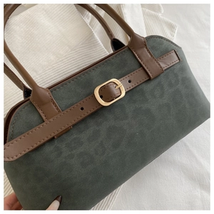 Close-up of dark green suede handbag with brown leather strap and gold buckle detail