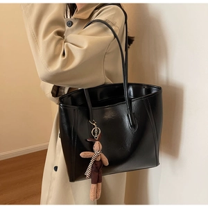 Detail of black leather tote bag with cute plush rabbit charm on a beige trench coat