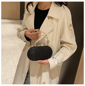 Detail of black glitter evening clutch with gold ring handle and chain strap on model