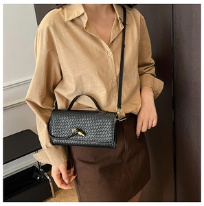 Detail shot of the black woven texture and gold metal lock on this stylish crossbody bag