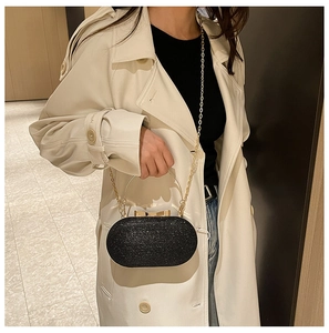 Detail of black glitter evening clutch featuring a gold ring handle and metal chain strap