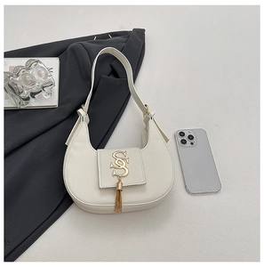Detail view of cream crescent bag with golden SS logo and chain tassel accents