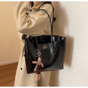 Detailed view of black tote bag with cute bunny charm on a beige trench coat