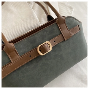 Close-up of retro green suede tote bag featuring brown leather straps and gold buckle detail