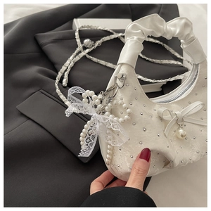 Close-up of white pleated cloud bag with silver rivets and pearl lace bow charm