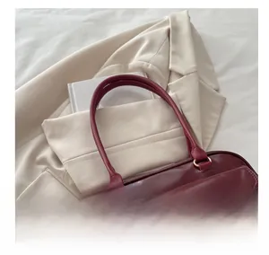 Detailsicht der burgunderroten Lederhandtasche mit goldenen Beschlägen und Tragegriff