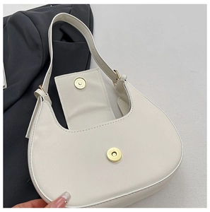 Detail view of the golden magnetic closure on the minimalist white crescent shoulder bag