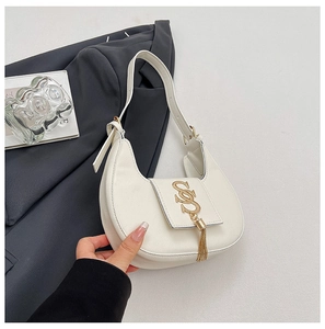 Detailed view of a white crescent shoulder bag with golden metal logo and tassel accents