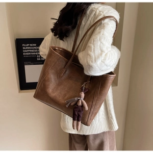 Detail view of large brown retro tote bag with a cute bear charm and leather texture