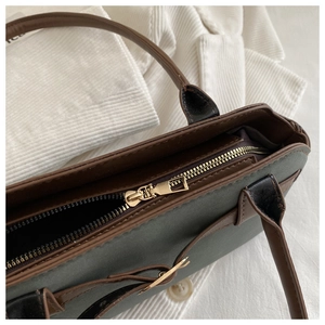 Detailed close-up of golden zipper closure and brown strap on green faux leather bag
