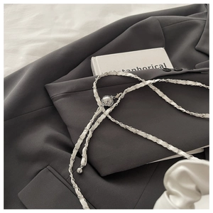 Detail of white leather interwoven with silver metal chain and ball charm on grey fabric