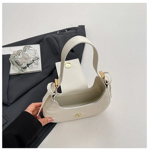 Detail of minimalist cream-white crescent bag with gold magnetic buckle and smooth leather