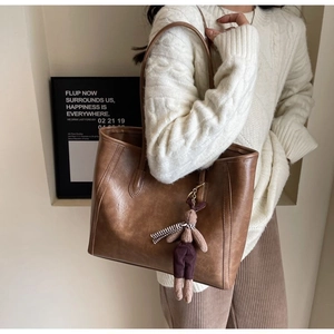 Detail of vintage brown leather tote bag with a cute rabbit charm in an urban setting
