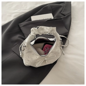 Close-up of white pleated handbag with silver studs and pearl bow detail in a lifestyle setting
