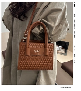 Close-up of brown quilted handbag with metal bow clasp worn with a beige trench coat