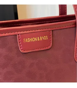 Detail of fashion bags logo and stitching on dark red suede textured tote bag