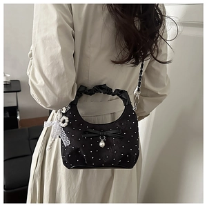 Detail of black polka dot handbag with bow and pearl charms worn over a beige trench coat