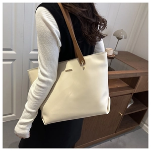Detail view of a minimalist cream tote bag with slim brown straps shown on a model