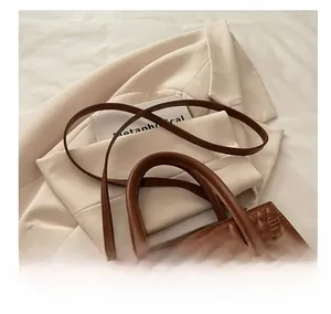 Detail of dark brown quilted PU handbag with gold bow buckle on beige blazer