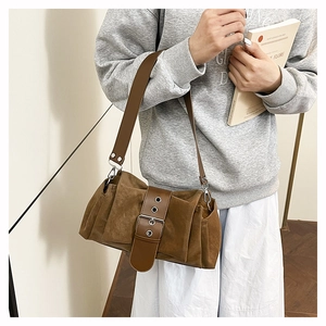 Détail d'un sac à bandoulière en daim marron avec une grande boucle et des œillets argentés