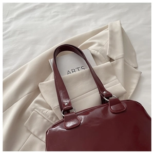 Close-up of wine red patent leather shoulder bag on a cream blazer with silver rings