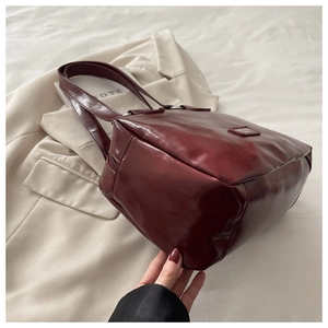 Detail of burgundy glossy leather handbag texture on beige blazer background