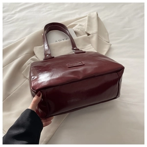 Detail of burgundy glossy leather tote bag with elegant brand logo and refined texture