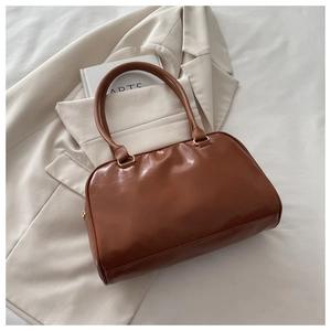 Detailed view of a vintage brown leather Boston handbag placed on an off-white blazer