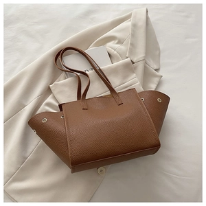 Detail of a brown lychee pattern leather tote bag with silver eyelets and slim handles