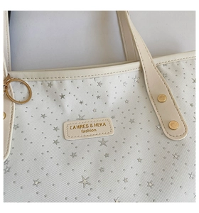 Gros plan d'un sac cabas beige avec étoiles argentées et étiquette de marque en cuir