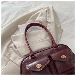 Macro detail of wine red PU leather handbag with dual front pockets and gold turn-lock clasps