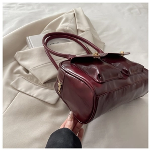 Detail of burgundy patent leather shoulder bag with gold twist locks on front pockets